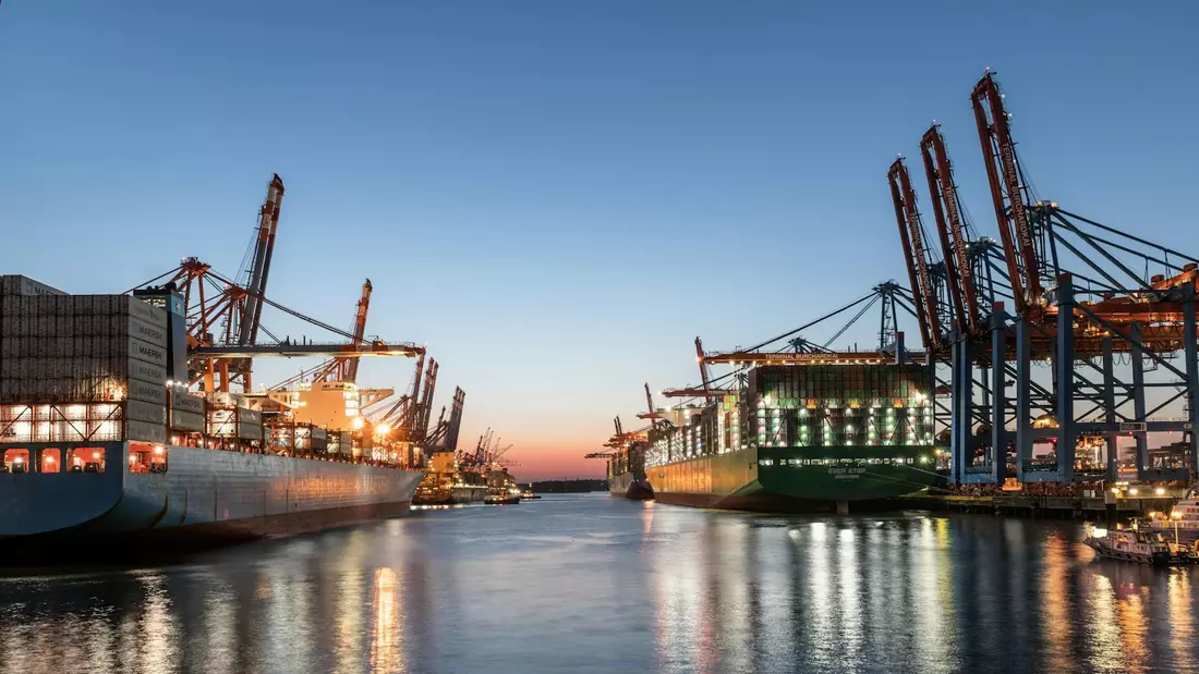 Container ships berthed under ship-to-shore cranes at a port terminal at dusk